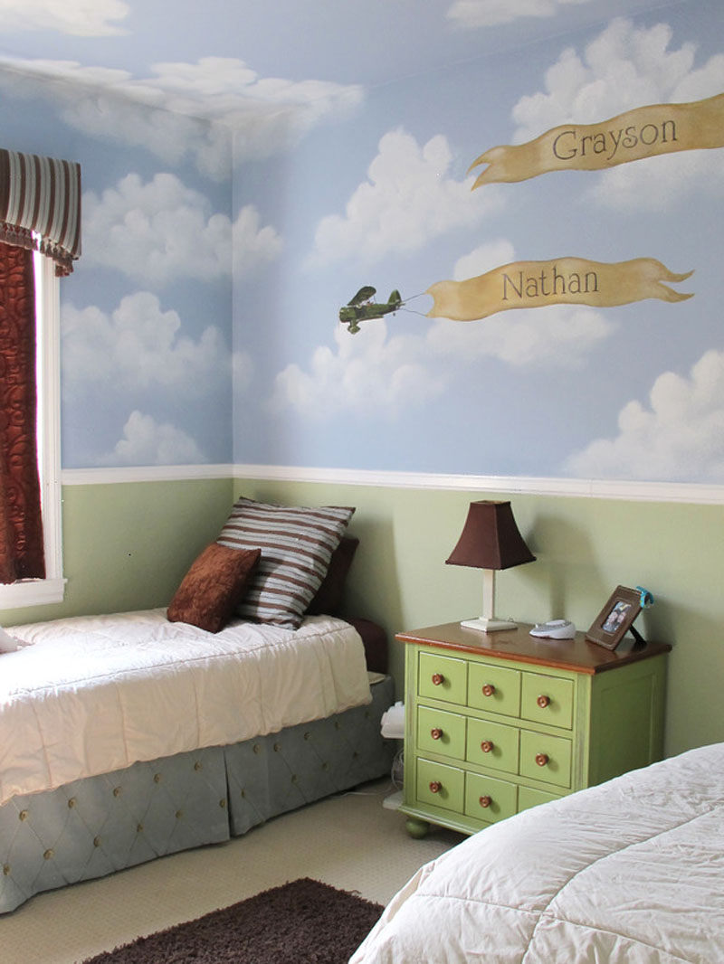 Kids room with blue sky and white clouds painted on wall and ceiling, double twin beds, green side table with small drawers.