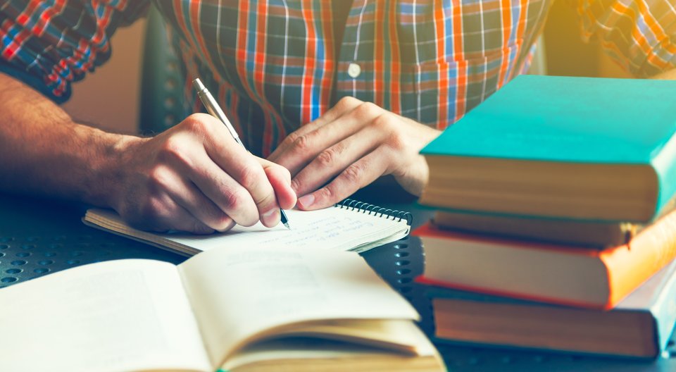 essay-writing-behind-a-pile-of-books 14 Ways to Improve Your Grades if You're Underperforming